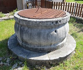 An old cistern: it is a squat, rounded concrete cylinder built into the ground, with a cover, roughly a bit less than 2 meters wide.