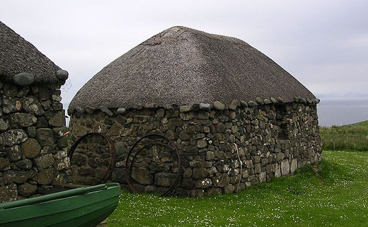 A stone cottage on a green grass lawn, with the sea in the background.