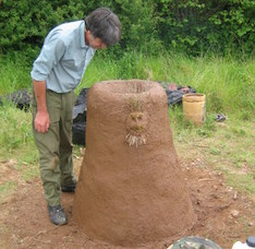 A simple cylindrical furnace made of red clay, a bit more than a meter tall, with a human face moulded onto the side for decoration.