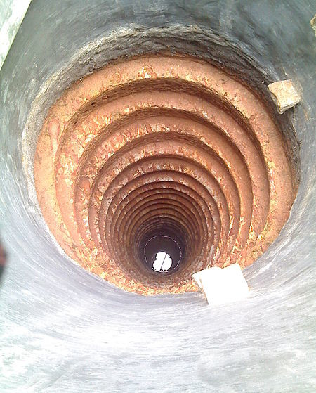 Photo: view down into a narrow water well made from rings of some brown-red material.